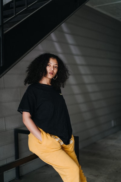 Dressed in a black T-shirt and a yellow skirt woman standing in front of the gray walls
